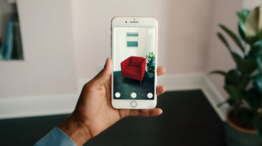 hand holding a phone in their living room while using augmented reality to view a red chair in their home prior to purchase