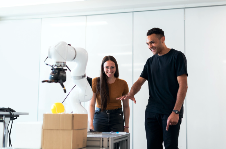 man and woman interacting with robotic arm that sorts a yellow object into a box 